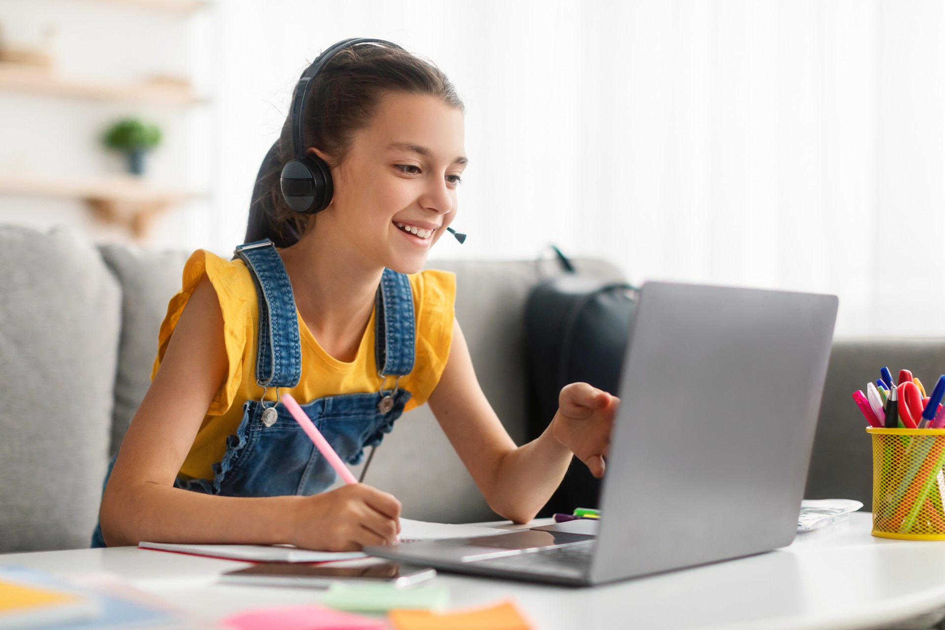 Cheerful girl sitting at table, using laptop, talking to webcam